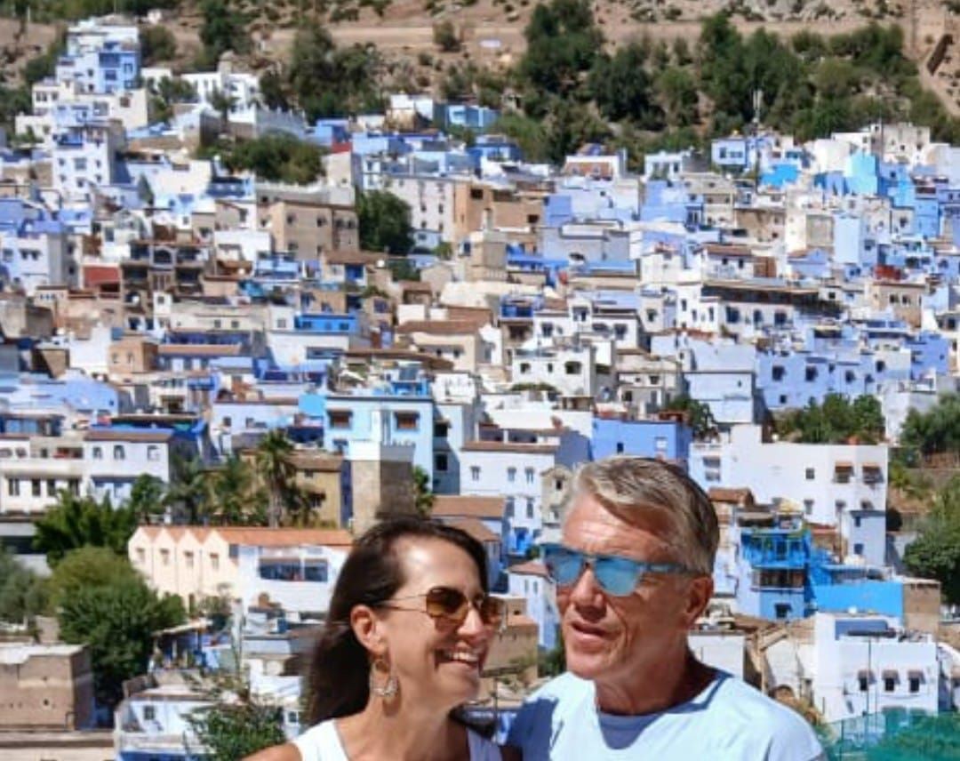 A scenic view of the Rif Mountains during a day trip from Tangier to Chefchaouen, showcasing the picturesque blue buildings of Chefchaouen nestled in the mountains, with a car on the winding road symbolizing travel options